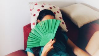 A woman holding a handheld fan covering her face