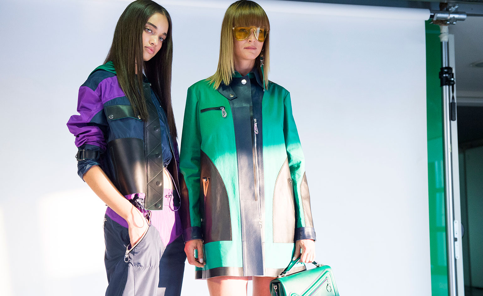 Model wearing green, purple and black color jacket and holding handbag