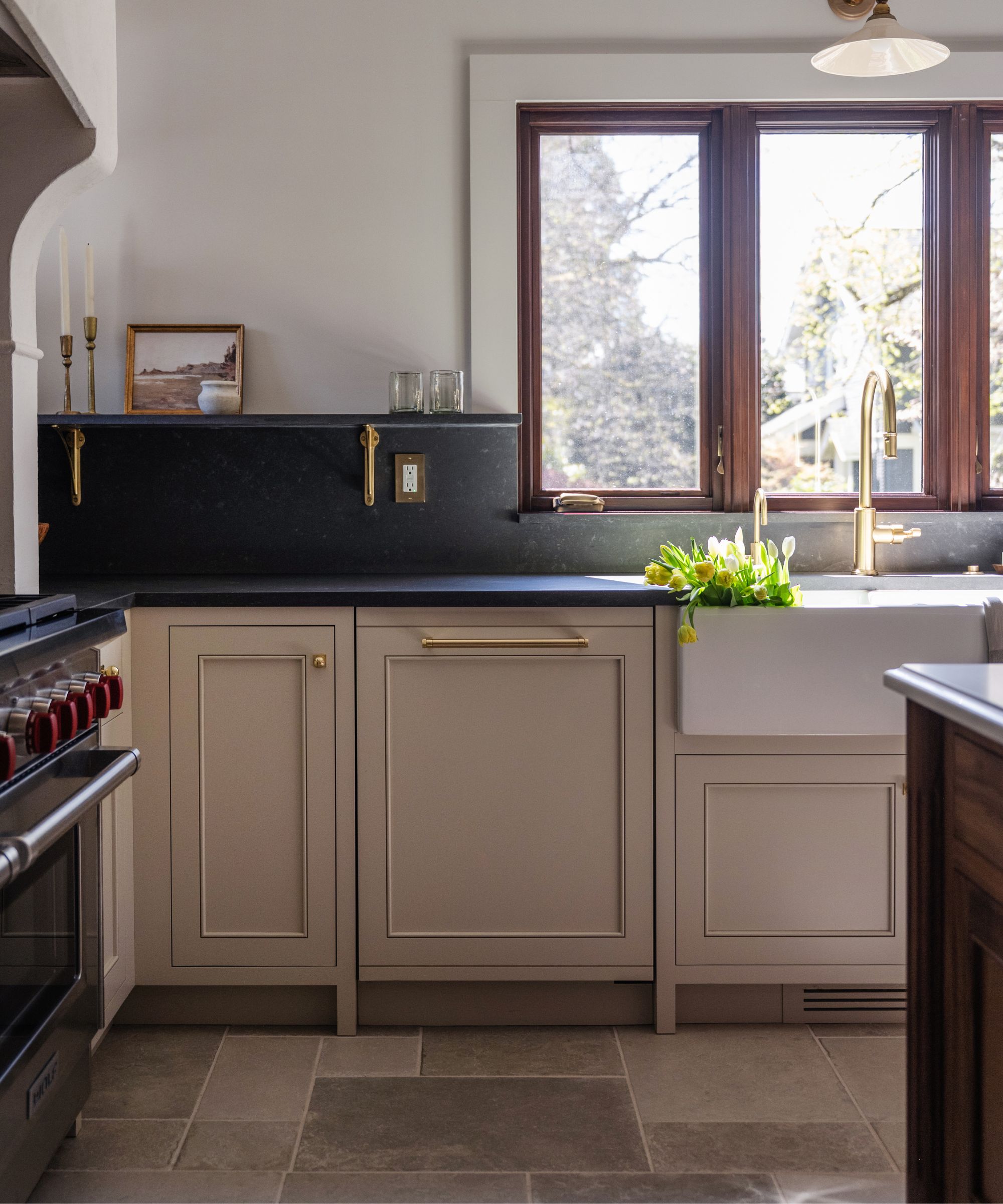 A neutral arts and crafts kitchen with black countertops and warm-toned tile floors