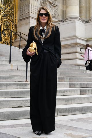 Anna Dello Russo wears black sunglasses, golden leather bag, black jacket, black Loewe pants outside Zimmermann during its womenswear fall/winter 2025/2026 show during Paris Fashion Week on March 10, 2025.