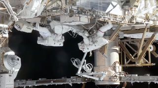 two astronauts in white spacesuits work outside a space station