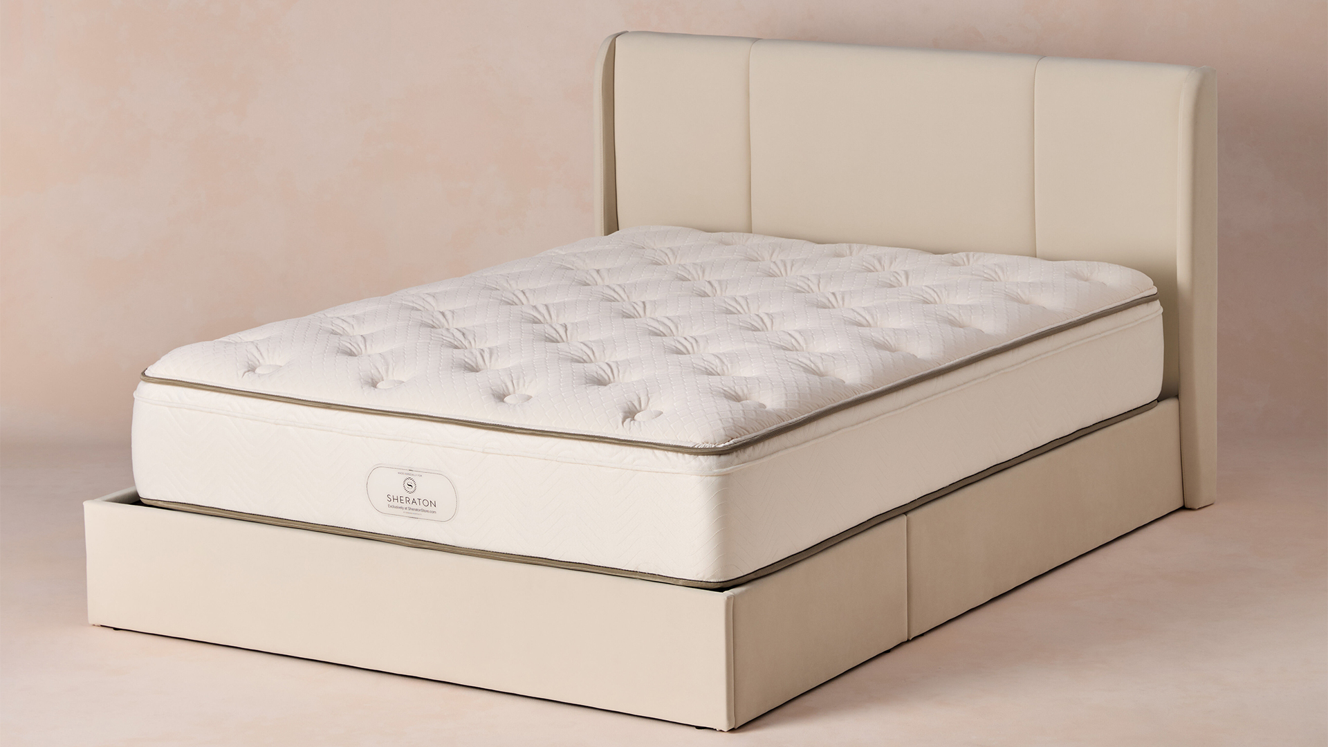 The Sheraton Hotel Mattress on an upholstered bed frame in an empty room with a peach colored background