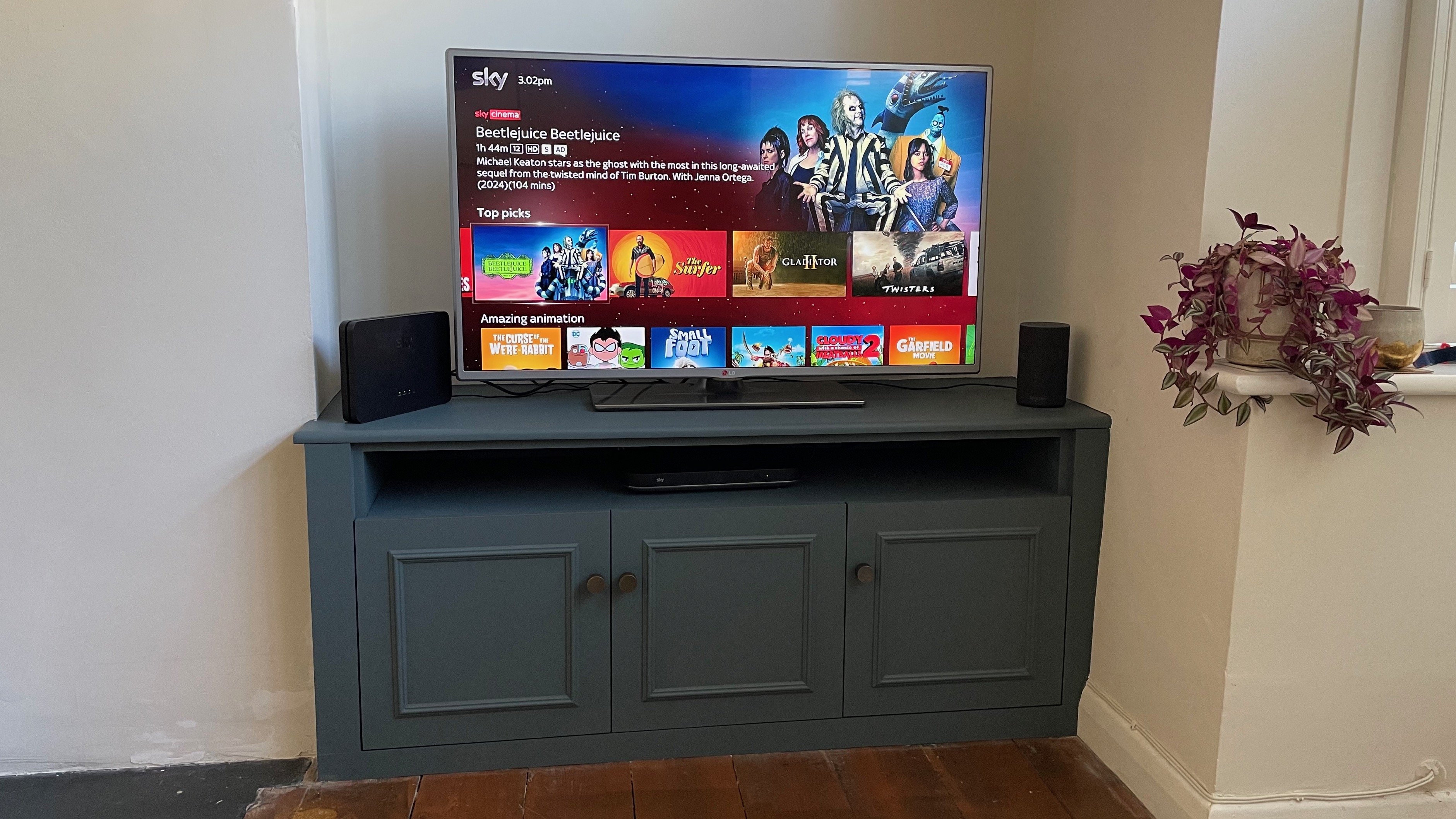 A dark blue TV cabinet with a TV on it, shot straight on. On screen is the Sky menu showing Beetlejuice Beetlejuice.