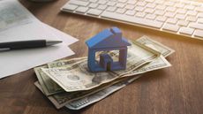 A model of a house sits on a stack of $20 bills in front of a computer.