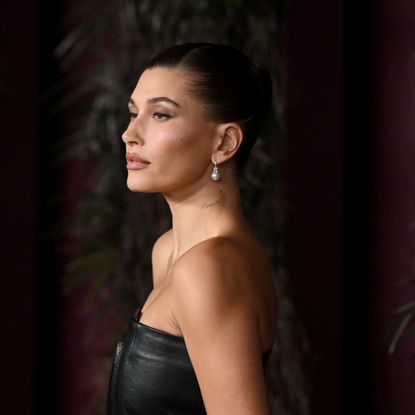 a white woman with dark hair posing in a black, strapless dress in front of a dark background on a red carpet