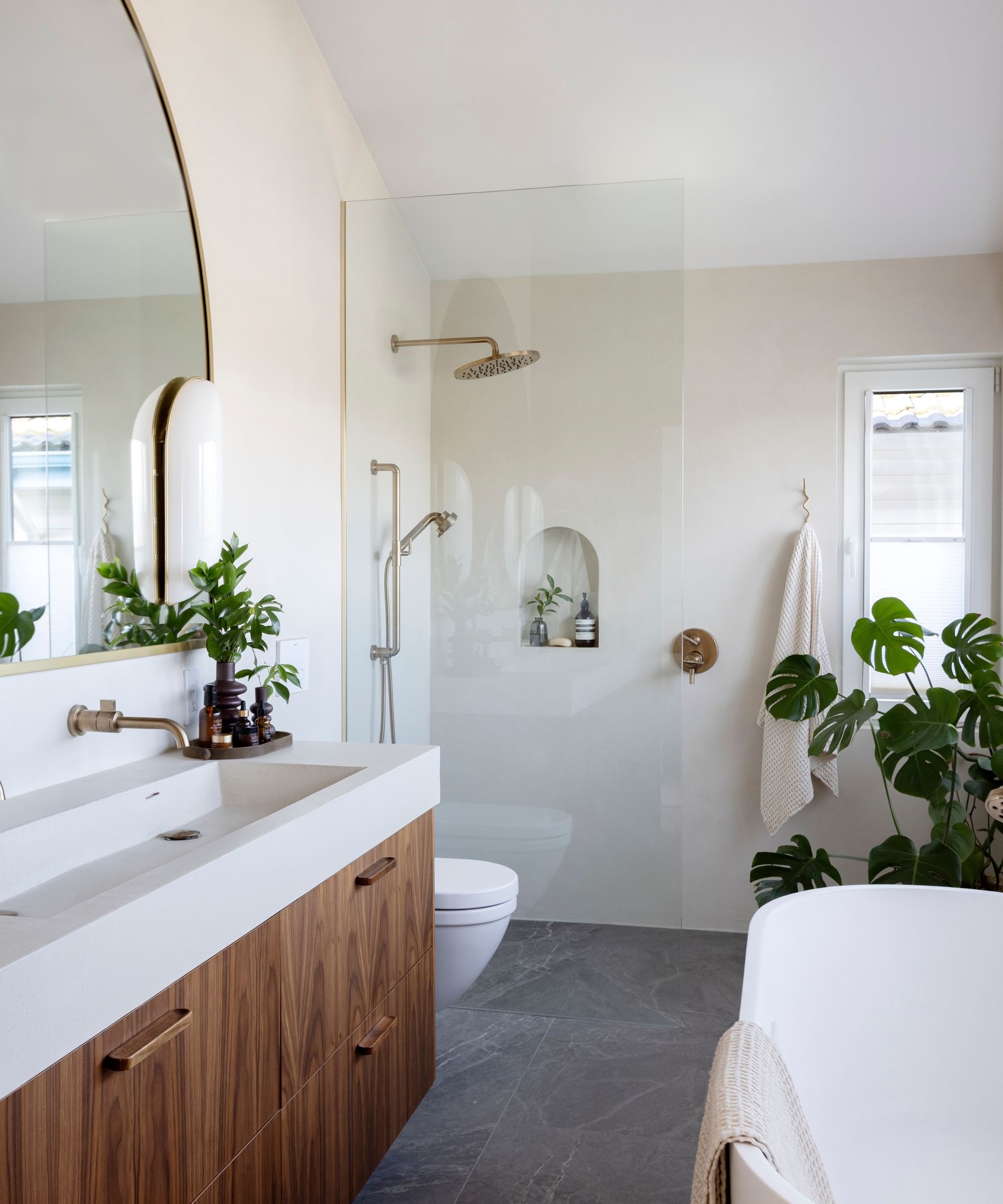 A neutral bathroom with warm white walls, a glass shower screen, a wooden vanity, and a microcement counter and sink