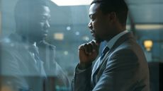 A businessman looks thoughtful as he looks through a window, his reflection staring back at him.
