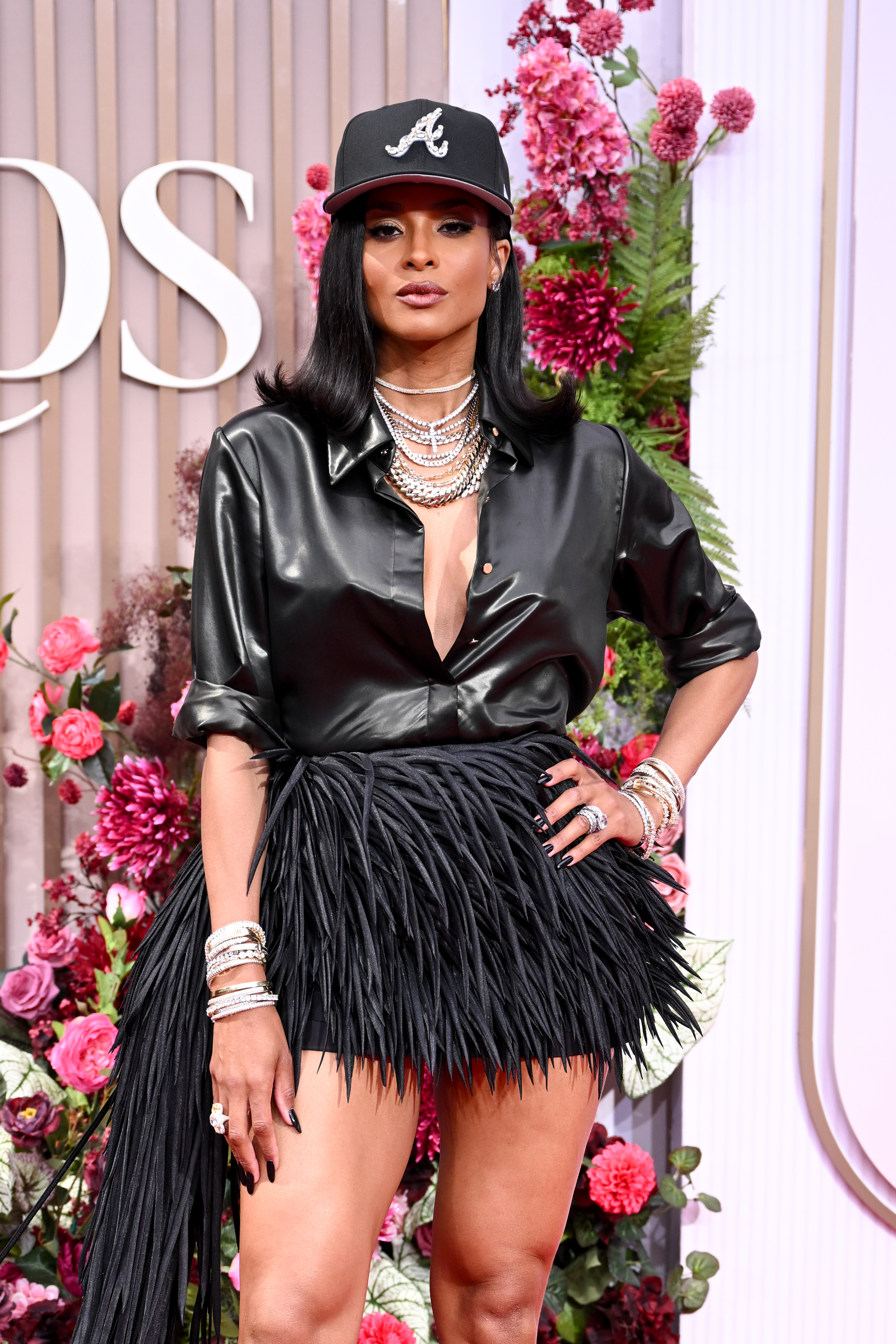 Ciara wearing a black leather button down and fringe skirt with a black baseball hat and silver jewelry.