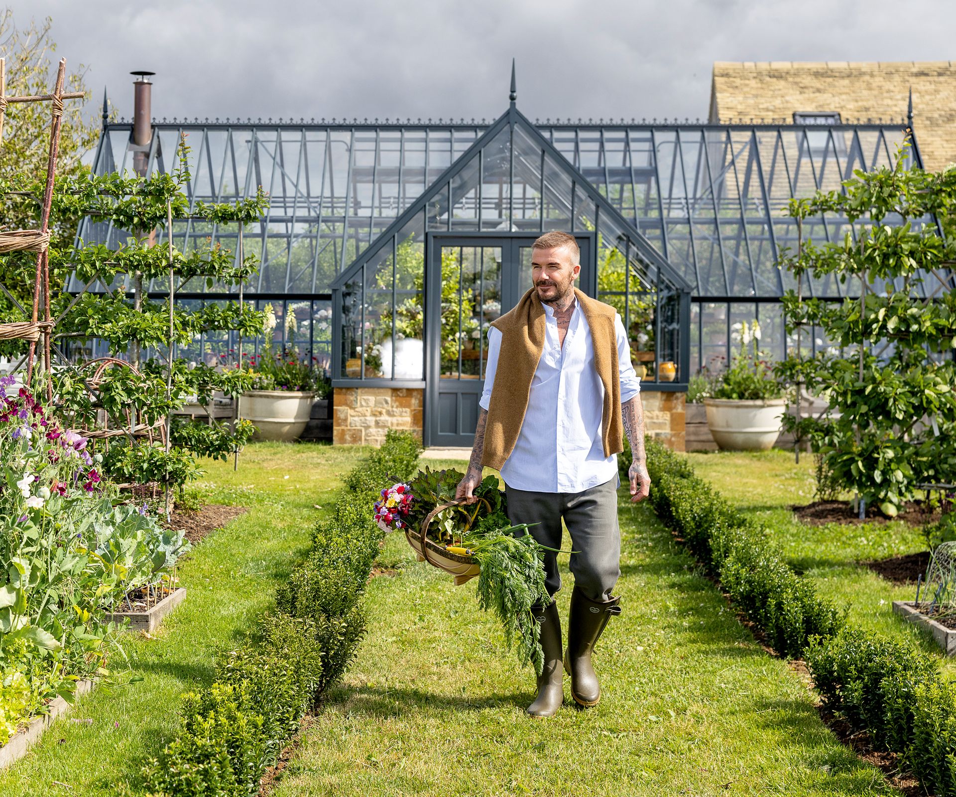 David Beckham carries his harvest in a basket in front of his greenhouse