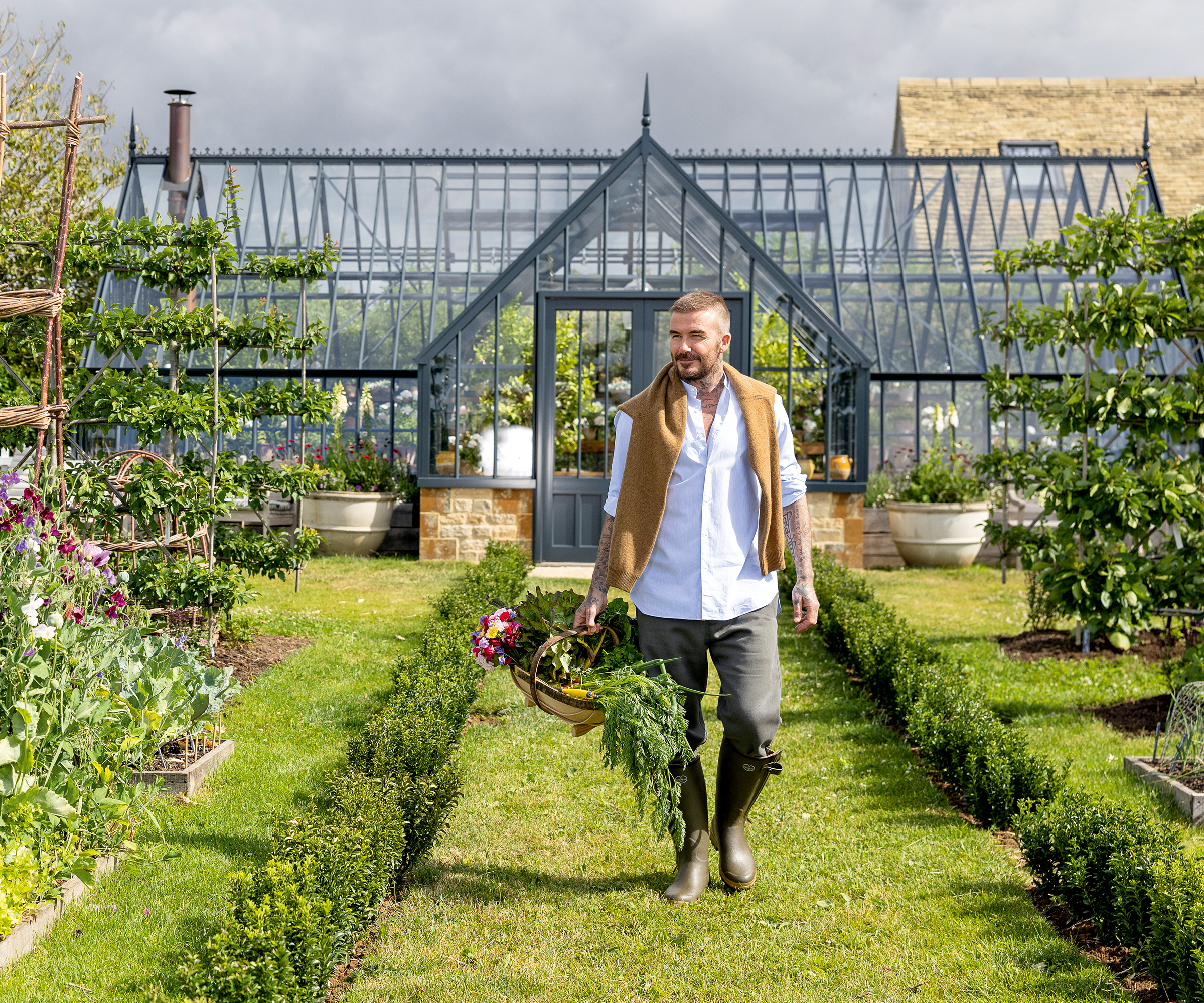 David Beckham carries his harvest in a basket in front of his greenhouse