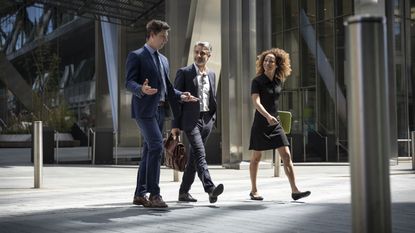Three business executives walk side by side outside the front entrance to a skyscraper.
