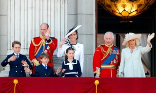 King Charles and Queen Camilla waving on the balcony of Buckingham Palace next to Prince William, Princess Kate, Prince George, and Prince Louis