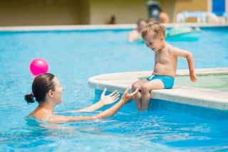 Cute boy with his mother playing in a pool