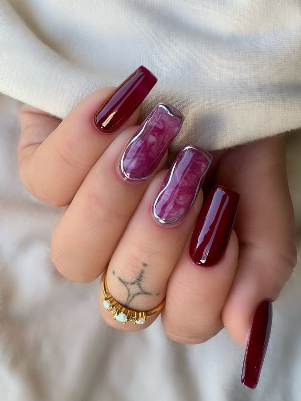 An image featuring a swirly burgundy nail design by @charlotteellennails