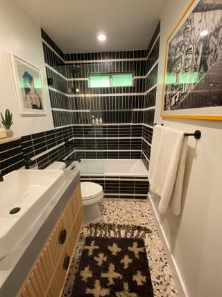 Black tiled shower with terrazzo floor and bathroom wall art