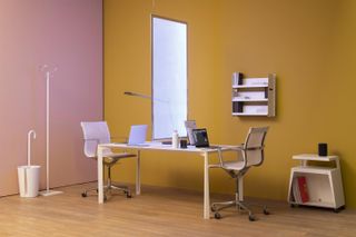 A set up of a working area, showing a white work desk with white office chairs. In the middle of the table, serving as a divider is a high, slim, and rectangle-shaped sanitation lamp that emits white light and UV rays.