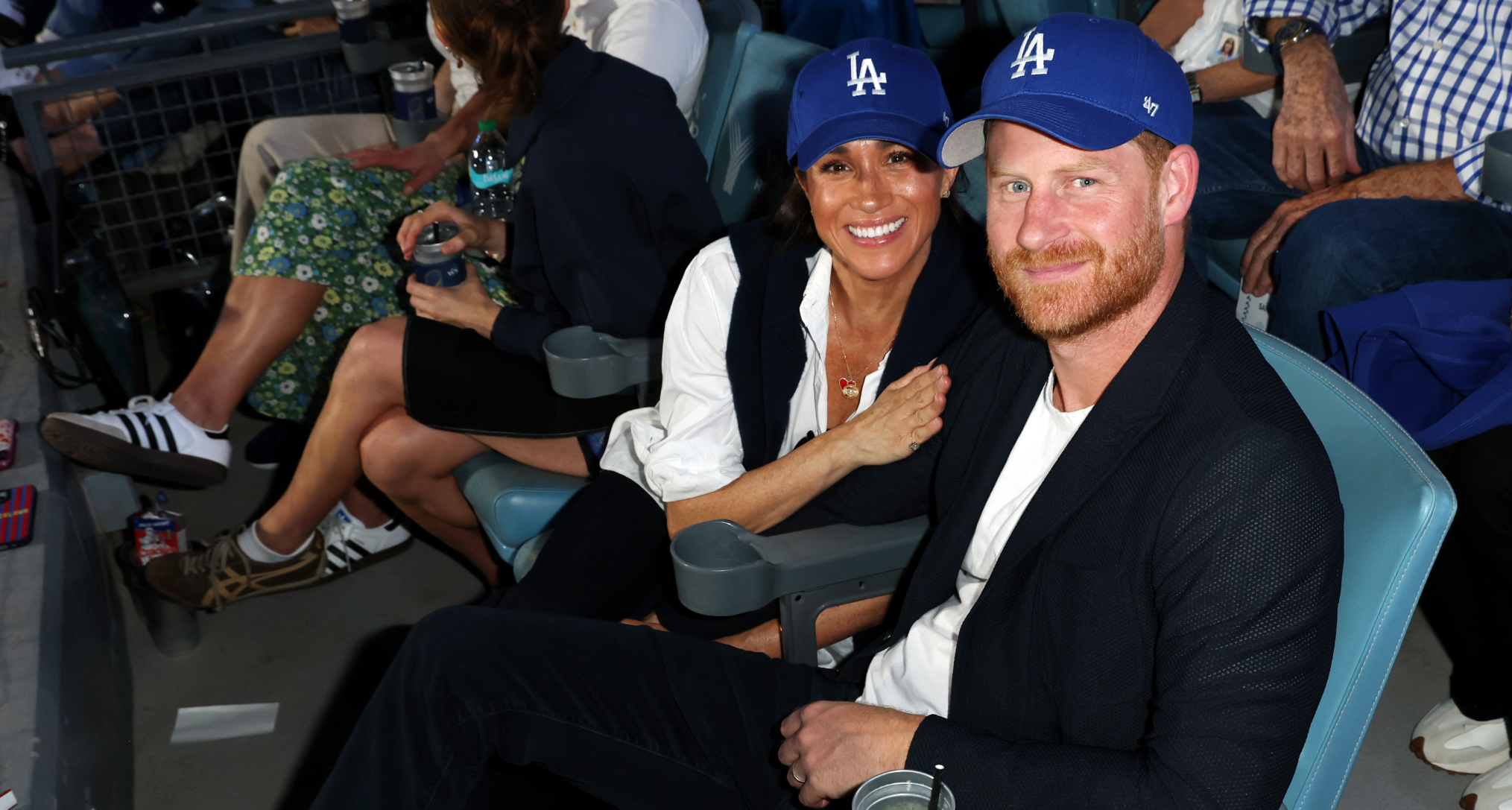 Meghan Markle holding Prince Harry's arm wearing LA Dodgers hats
