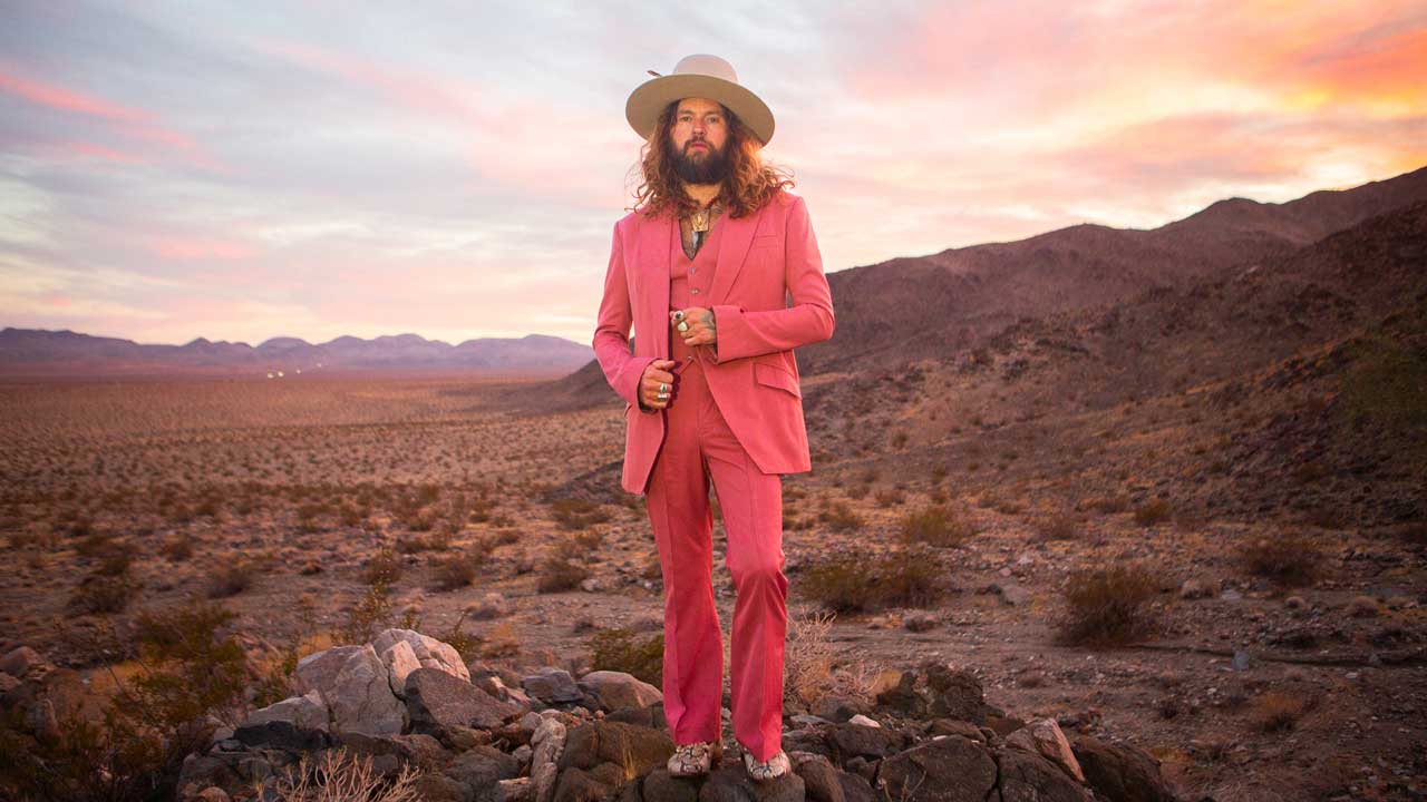 Jay Buchanan in a pink suit standing in a desert landscape