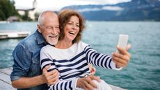 A senior couple smiling happily take a selfie near the beach.