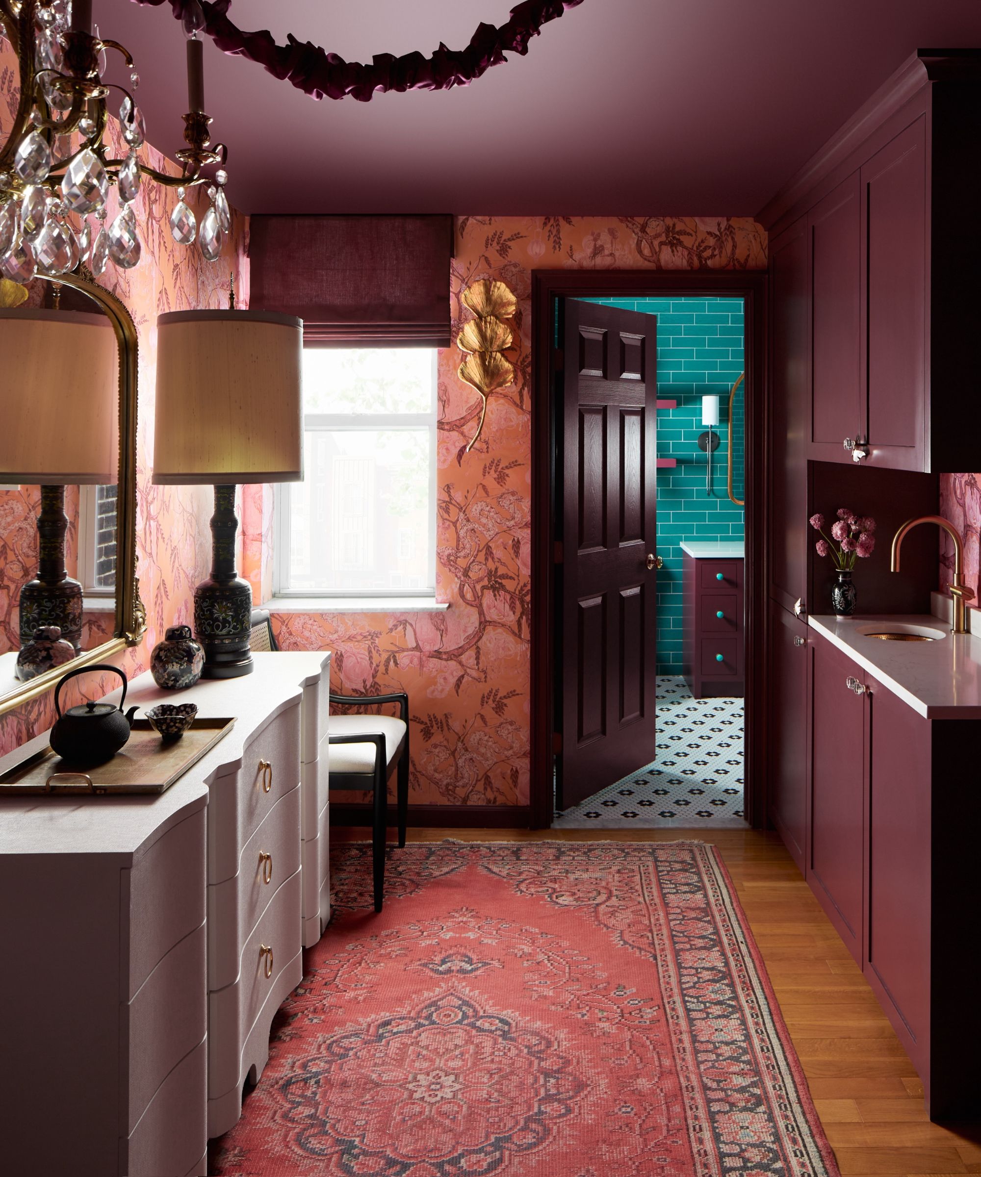 A small kitchen with plum-colored cabinets and ceiling, pink-patterned wallpaper, and wooden floors with a pink rug.