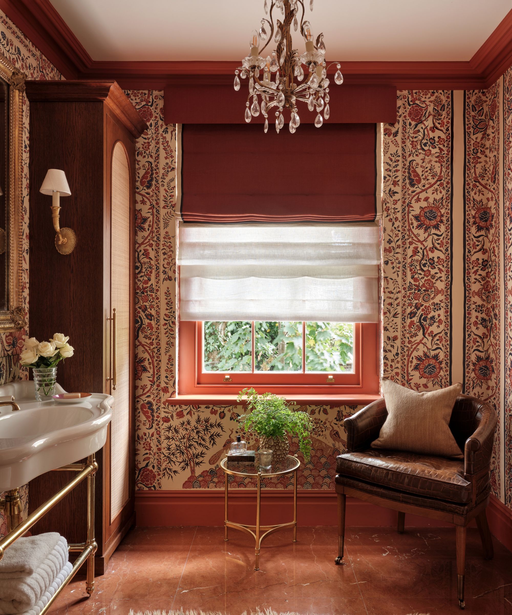A small bathroom with patterned wallpaper and deep red paint, and wooden built-in cabinets