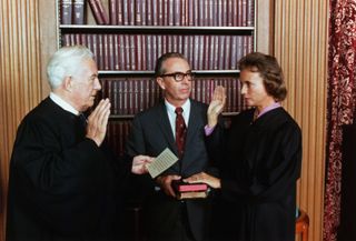 Sandra Day O'Connor is sworn in a Supreme Court Justice by Chief Justice Warren Burger. At center, holding two family Bibles, is her husband, John O'Connor.