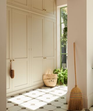 entryway with floor to ceiling cabinetry, patterned floor tiles, broom, basket, view of green painted crittall door