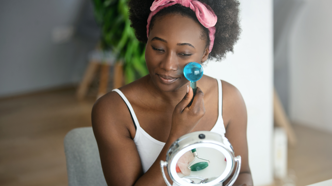 Skin Icing - black woman uses cryotherapy ice wands on her face looking into a mirror