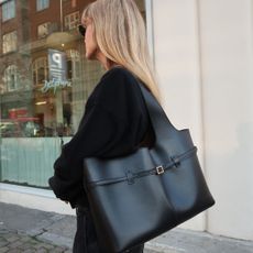 Woman wears black jumper, carries black leather tote bag
