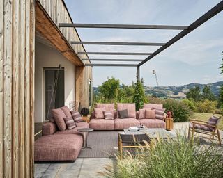An outdoor living area with a pink L-shaped sofa looking out onto scenic views