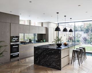 Grey kitchen ideas with wooden cabinetry and flooring, glass sliding doors and an island with black metal stools.
