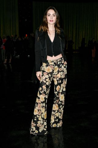 Lily Collins poses at the Saint Laurent Fall 2024 as part show during Paris Fashion Week held at Place Jacques Rueff on February 27, 2024 in Paris, France wearing a Saint Laurent jacket, vest top, and flared floral-print pants