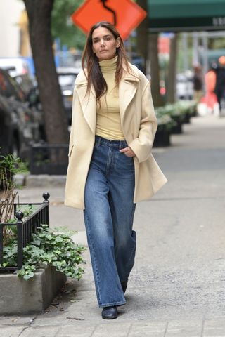 Katie Holmes wearing a yellow turtleneck, a double-breasted coat, jeans, and boots