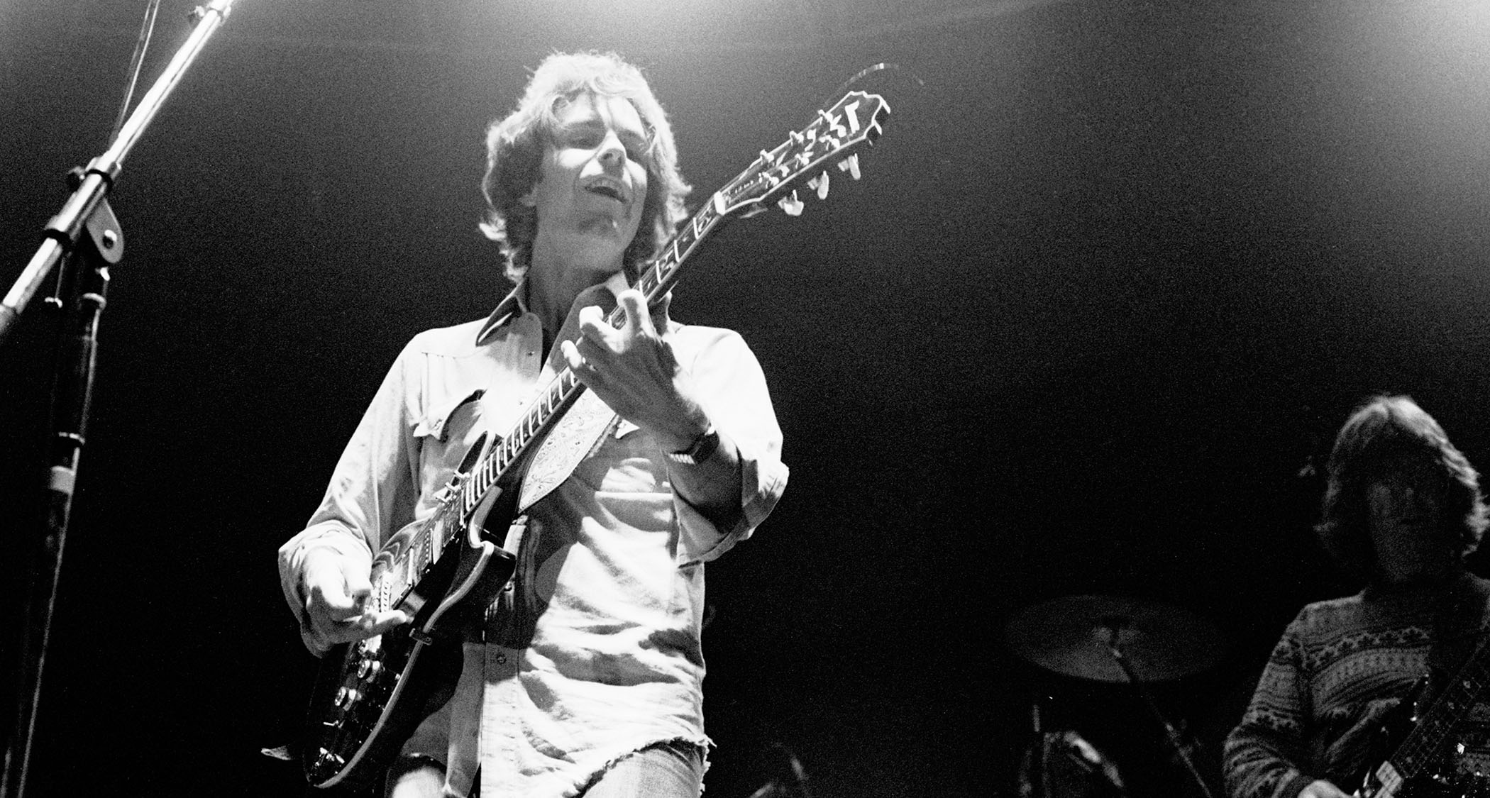 A black-and-white live shot of Bob Weir performing with the Grateful Dead in 1979, with Phil Lesh to his left.