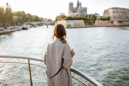 Young woman tourist enjoying beautiful landscape view on the riverside with Notre-Dame cathedral from the boat during the sunset in Paris