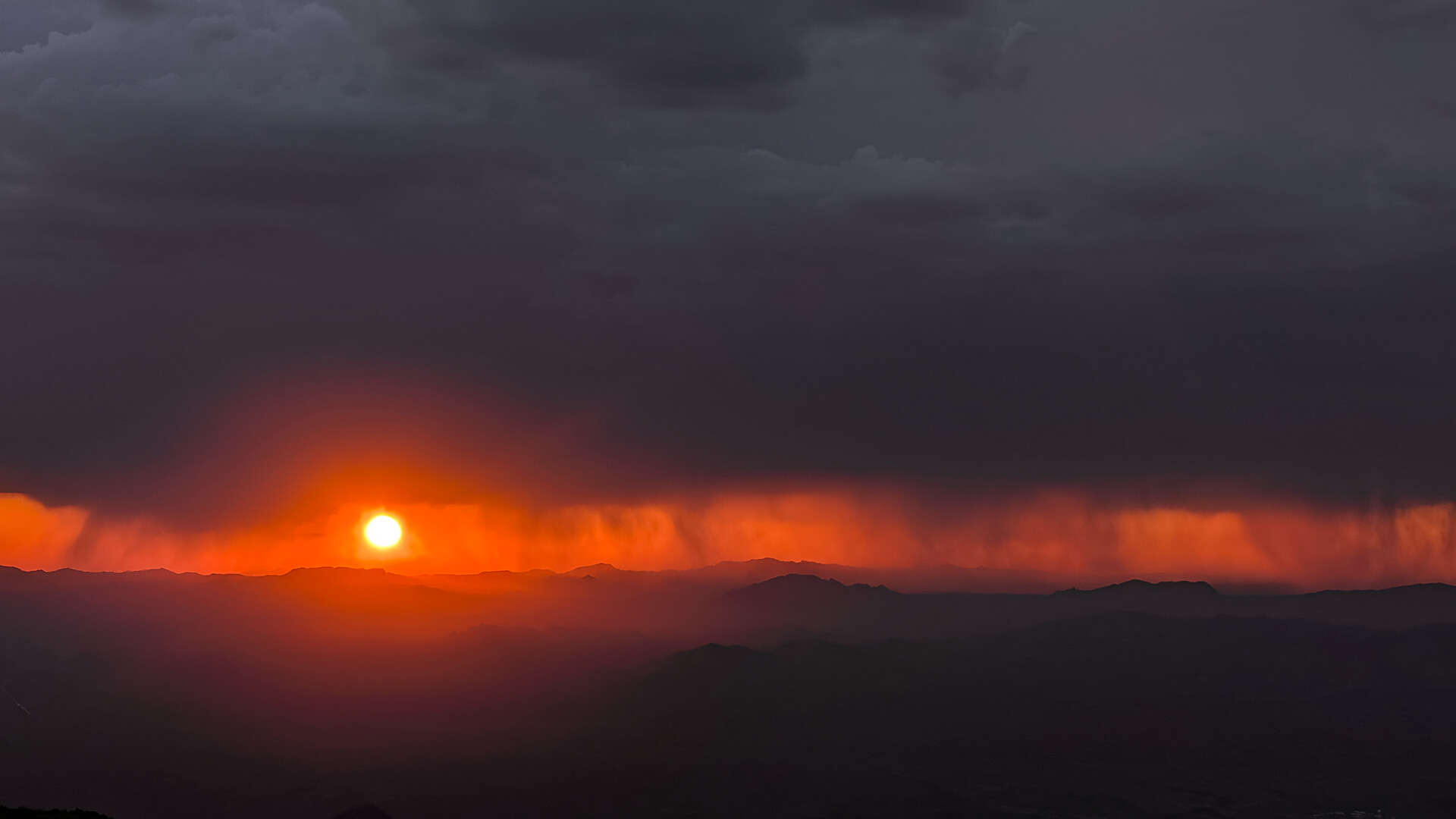 Gray clouds and a dark landscape sandwich a band of bright orange dusky sky during sunset