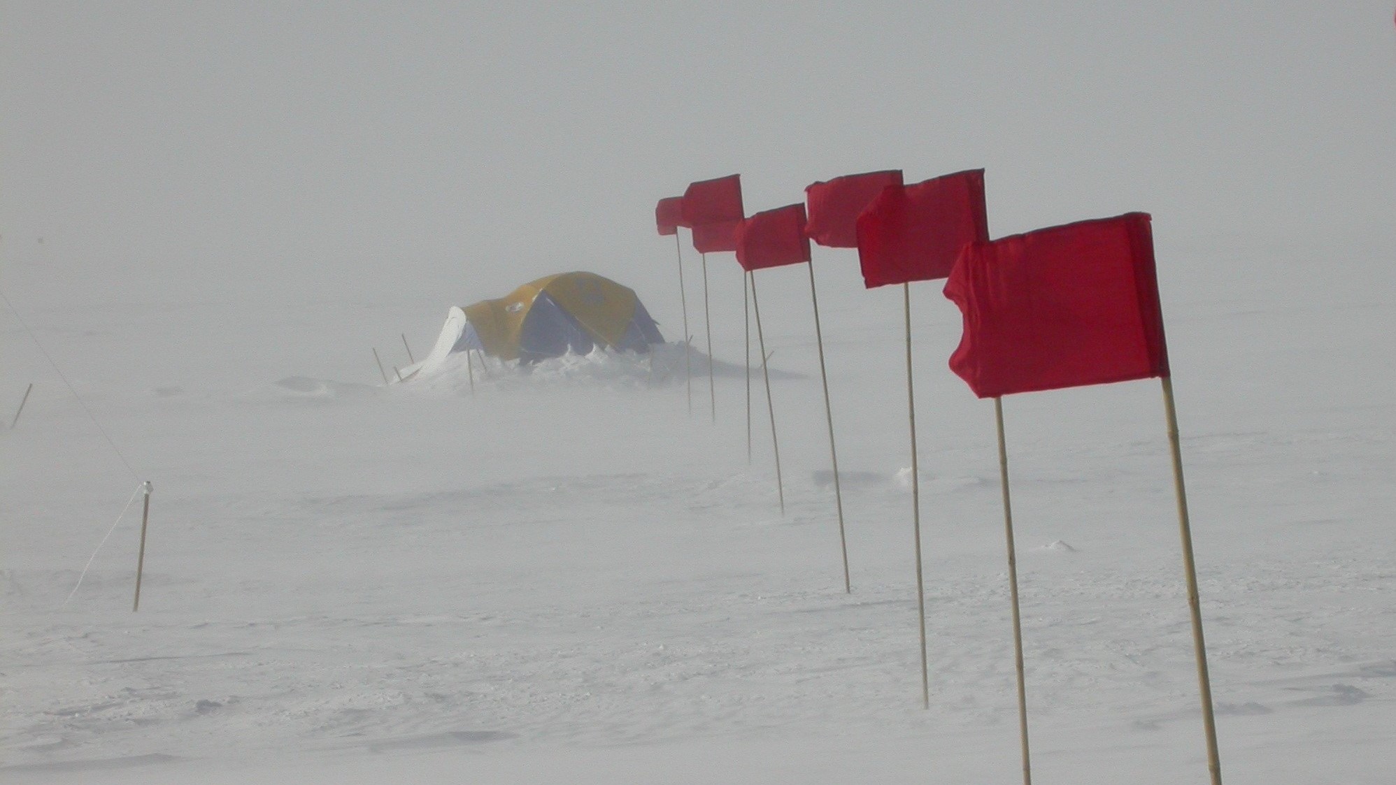 An igloo on an icy Antarctic plateau with red flags