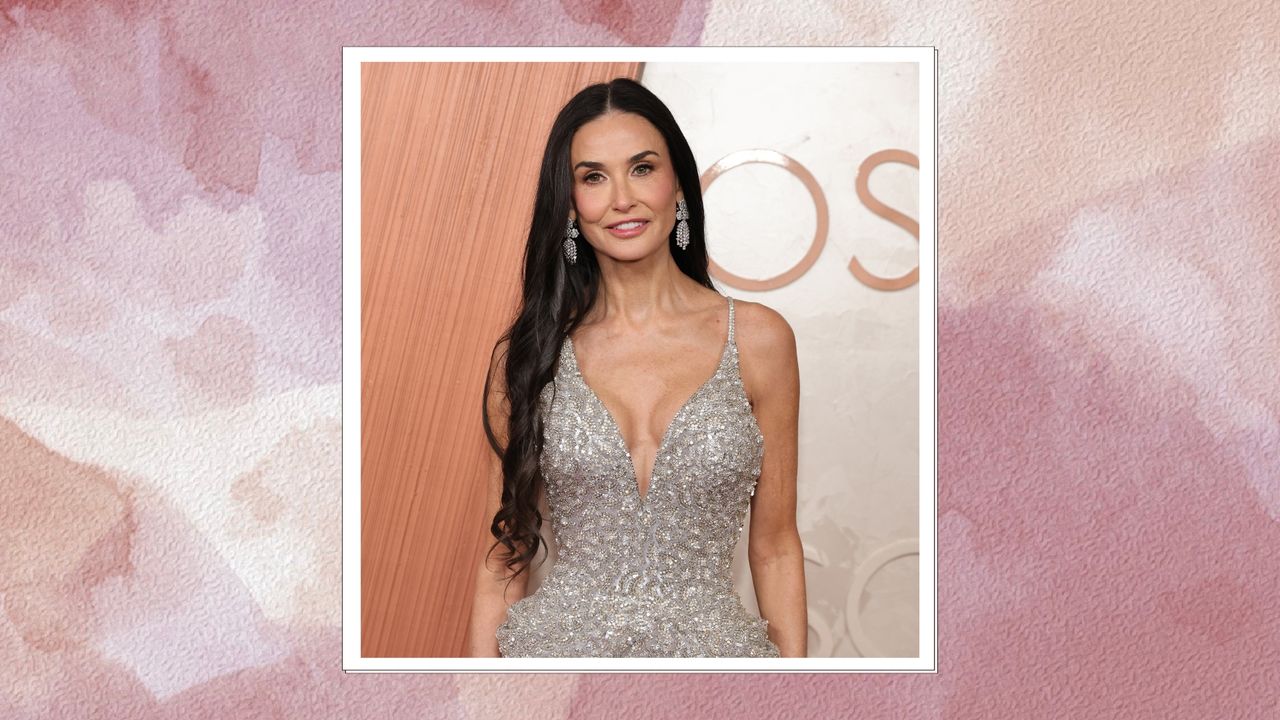 Demi Moore at the 2025 Oscars, smiling with long curled black hair and wearing a V-neck silver crystal-embellished gown, on a pink watercolour background