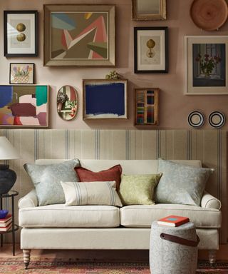 Pink living room with upholstered wall paneling in cream striped pattern, feature wall decorated with artwork and framed pictures, cream sofa with cushions,