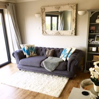 living room with cream colour wall grey sofa with designed cushion and mirror on wall