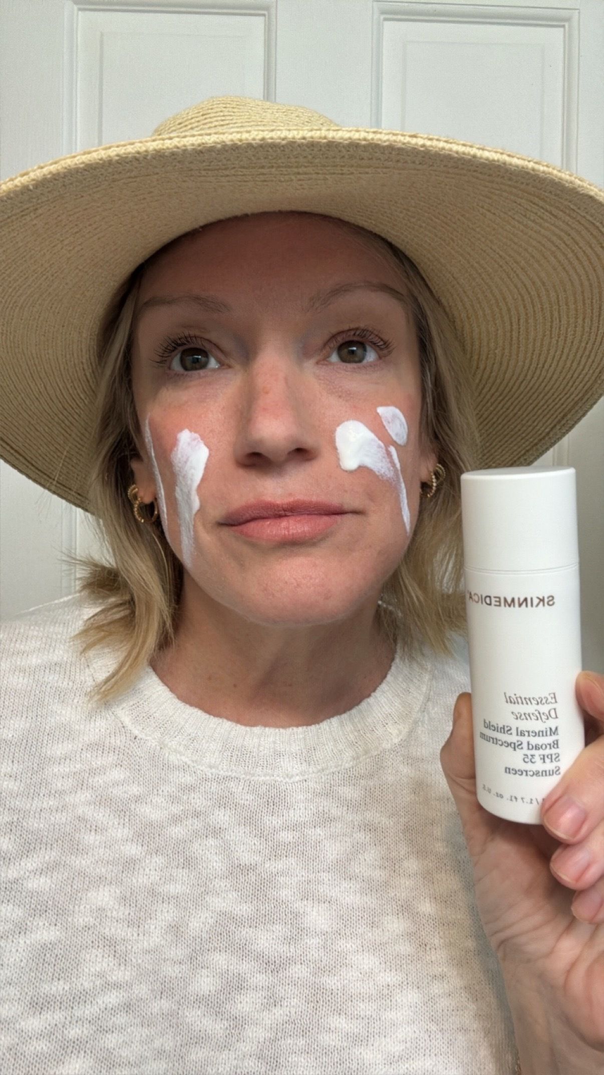 a woman with a tan sun hat and a white sweater before applying spf.