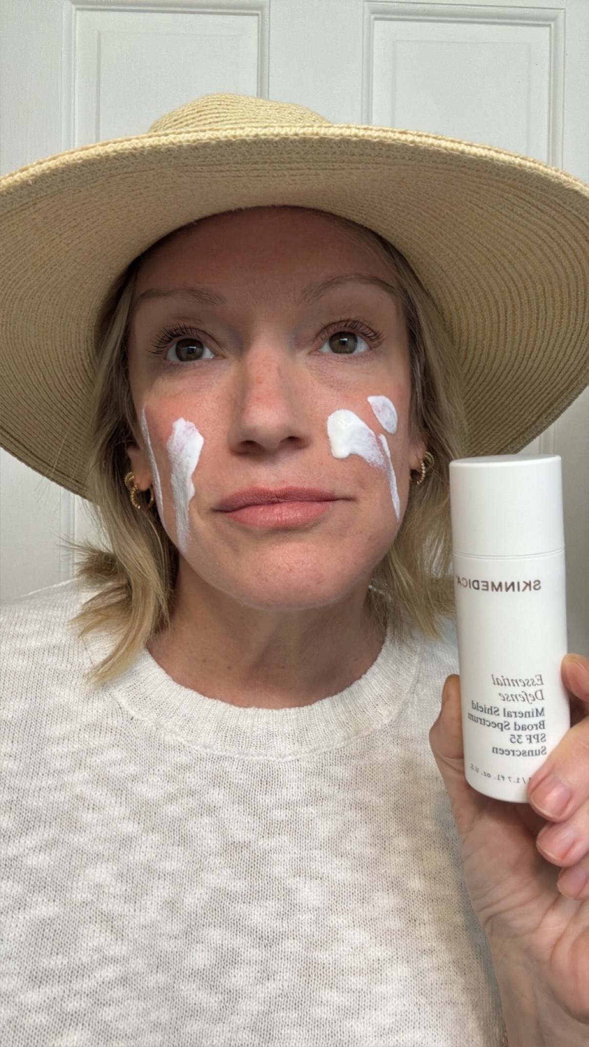 a woman with a tan sun hat and a white sweater before applying spf.