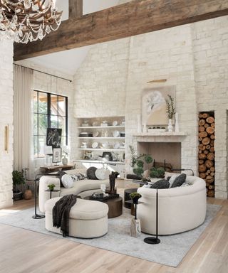 Double height neutral living room with facing curved sofas and footstool, coffee table, area rug, fireplace and shelves with decorative accessories