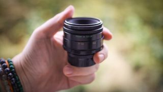 A hand holding the Helios 44-2 lens against a blurry woodland background