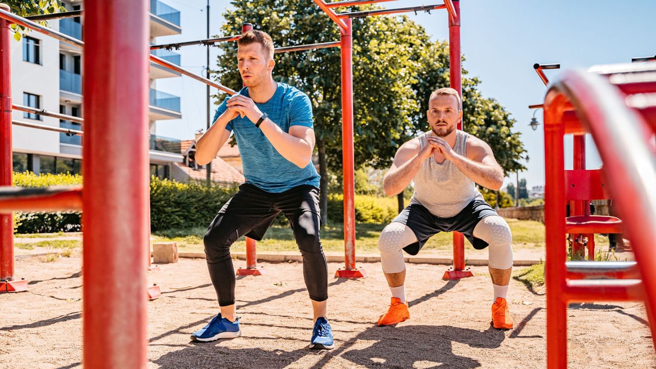 Two men performing squats as part of a bodyweight lower-body workout 