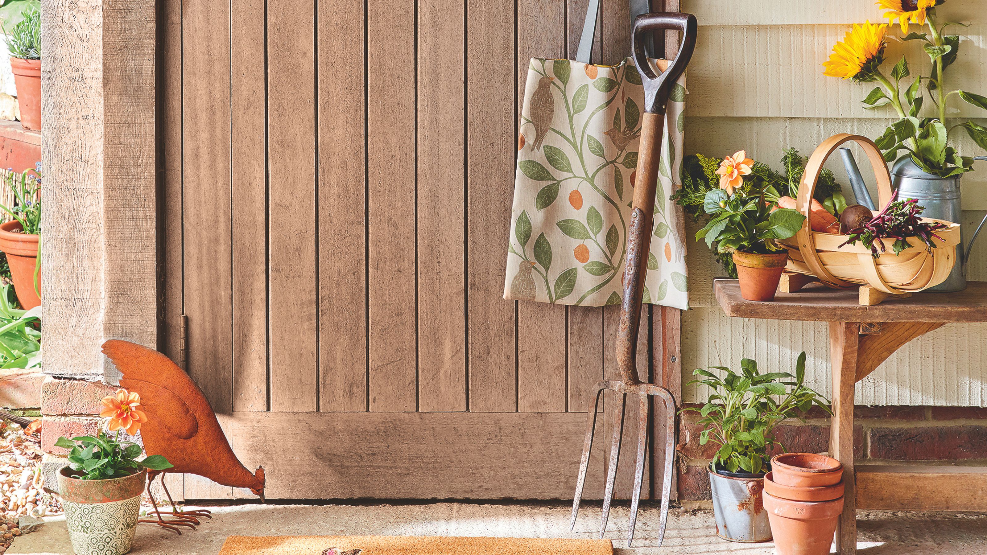 Garden fork resting against wooden door next to vase of sunflowers