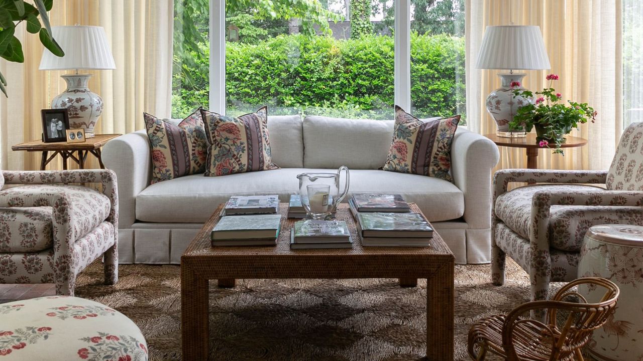 sunroom with a seagrass rug and a large white box pleate sofa with two floral arm chairs facing toward a large wood coffee table