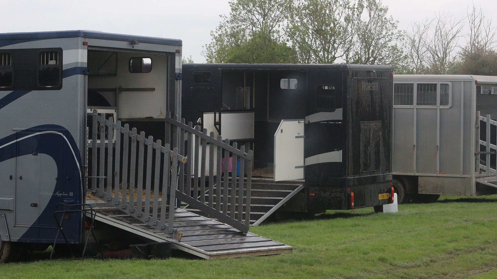 Horseboxes parked in a field with ramps down at a horse show.