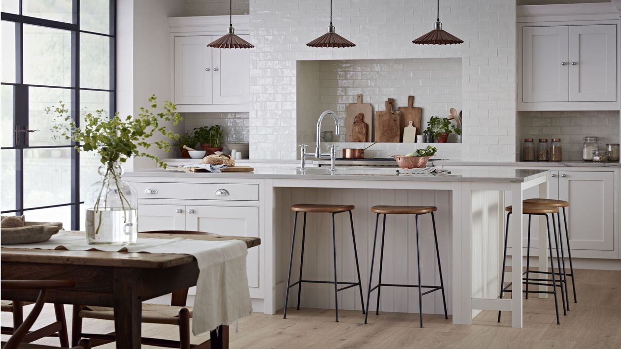 cream kitchen cabinets and island with wooden flooring, wooden dining table and 3 pendant lights 