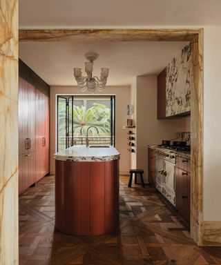 Kitchen with wooden flooring and rust colored curved kitchen island and marble details